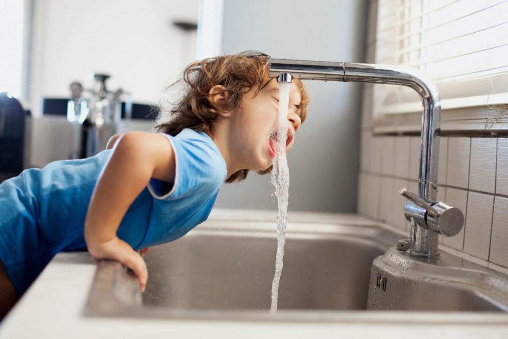 Een kind drinkt water uit de kraan.