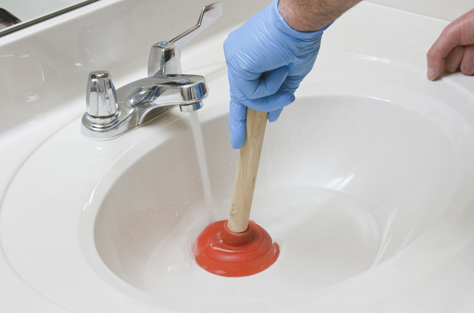 Removing a clog in the sink with a plunger.