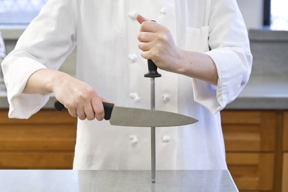 Um cozinheiro afia uma faca com musat.